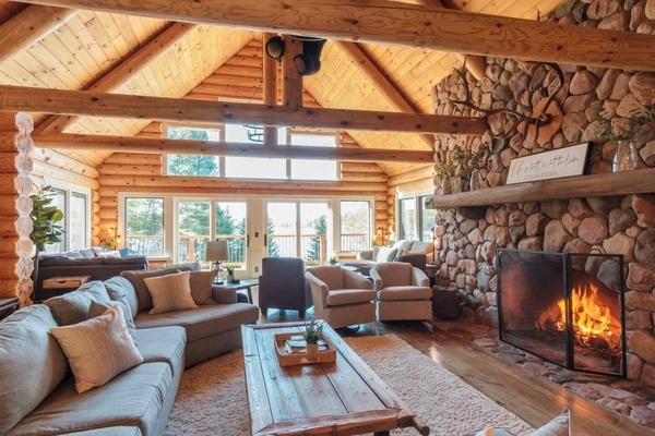 Interior great room with stone fireplace, vaulted wooden ceilings, leather sofas, and large windows
